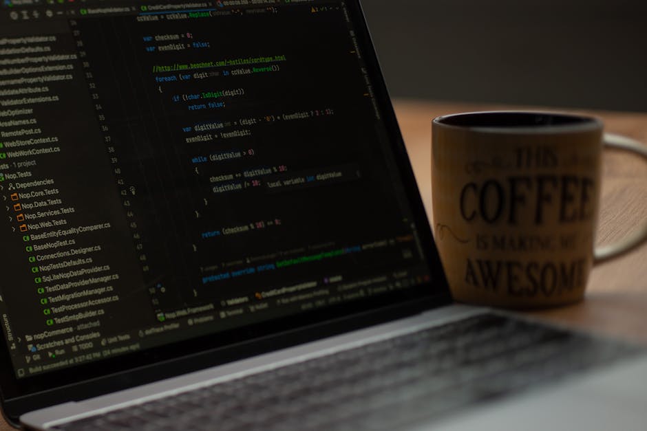 A close-up view of a laptop on a wooden desk displaying lines of code on the screen, with the HTML or programming language visible, alongside a ceramic coffee mug with the words 'This Coffee is Making